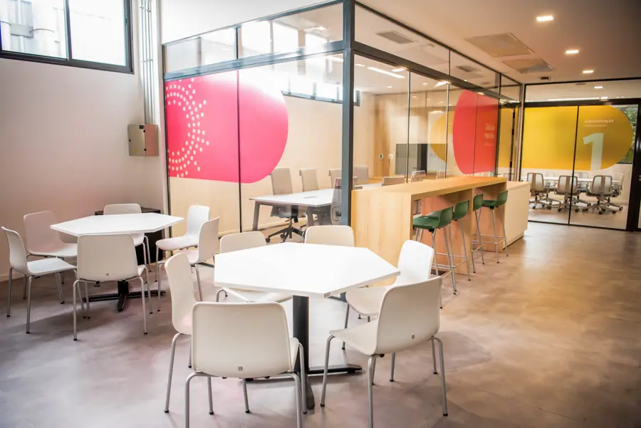 Salão com mesas e sala de reunião envidraçada com grafismos coloridos