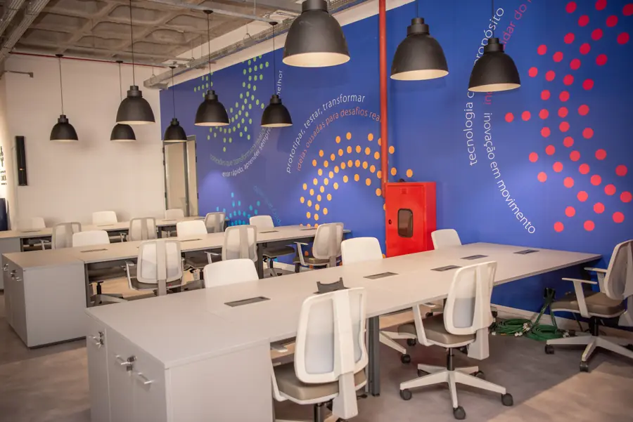 Área de trabalho compartilhada do HCPATec, com mesas brancas e o símbolo de pontos pintado na parede azul